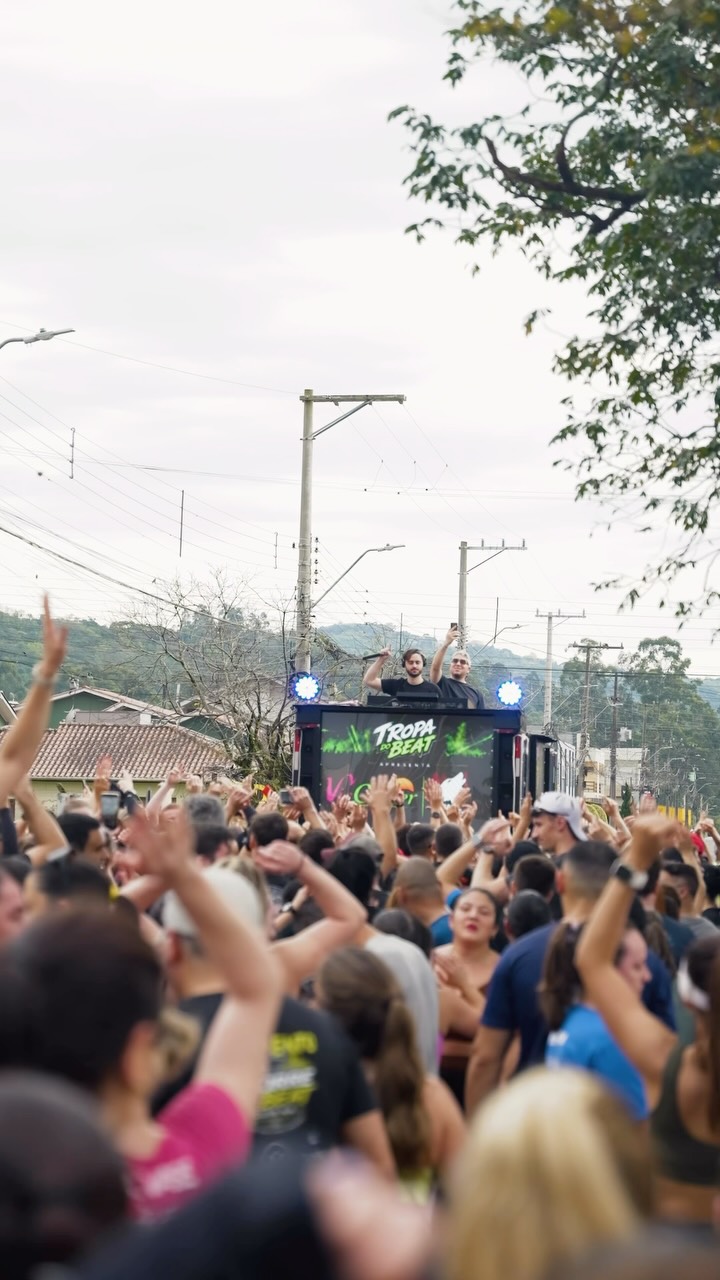 Pessoas da Tropa reunidas na rua, com as mãos para o alto e DJ tocando ao fundo